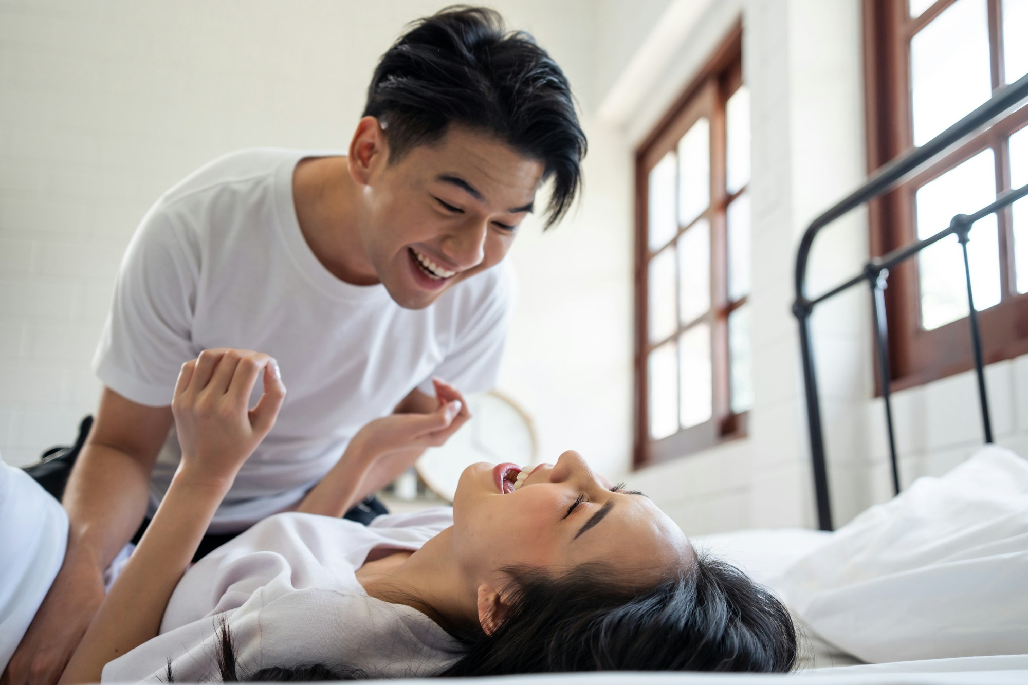 Asian attractive man tickles his girlfriend while lying down on bed.