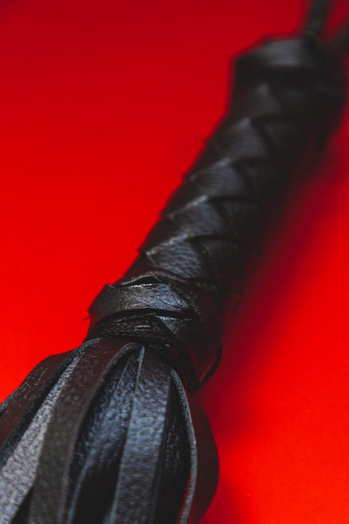 Histoire de cocu soumis depuis dix ans se fait humilié A detailed view of a black leather flogger against a striking red background, perfect for editorial content.
